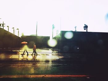 People walking on wet street against clear sky
