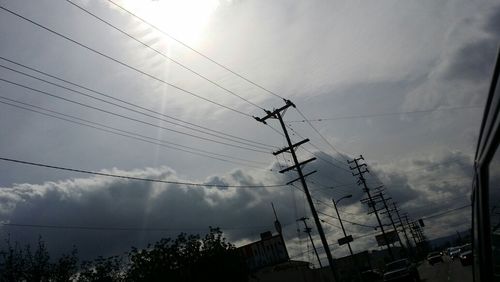 Low angle view of electricity pylon against cloudy sky