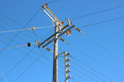 Low angle view of electricity pylon against clear blue sky