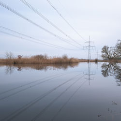 Electricity pylons by lake against sky