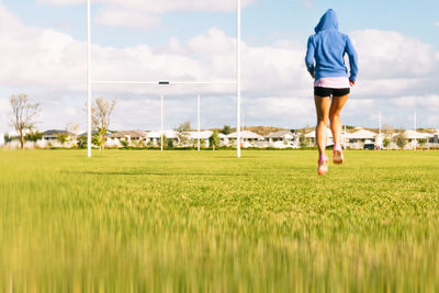 Rear view of woman jogging on field against sky