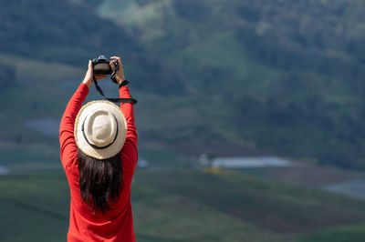 Rear view of woman holding hat standing against blurred background