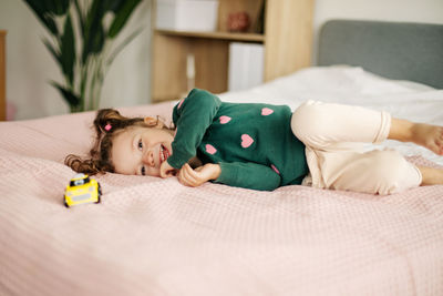 A charming little girl is playing with a car on the bed. home games, child development