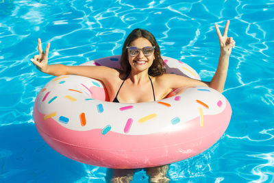 Smiling young woman enjoying in swimming pool with inflatable ring during summer