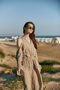 Young woman standing at beach against sky