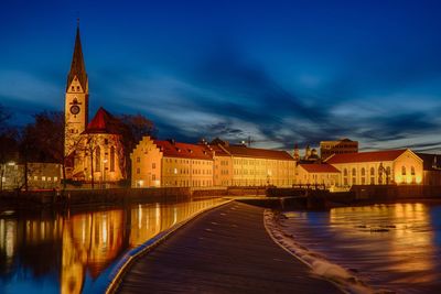 Illuminated buildings at waterfront against sky during night