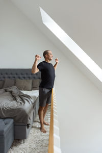 Male standing near bed and stretching arms after awakening in morning at home