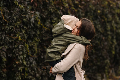 Happy mother and little son child walking in the autumn forest in nature in fall