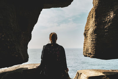 Woman looking at sea from cave against sky