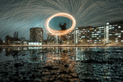 Man spinning wire wool while standing against illuminated city at night