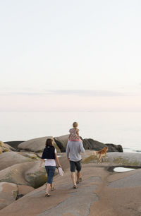 Rear view of man carrying girl on shoulder walking with woman against sky