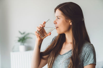 Young woman drinking bottle against wall