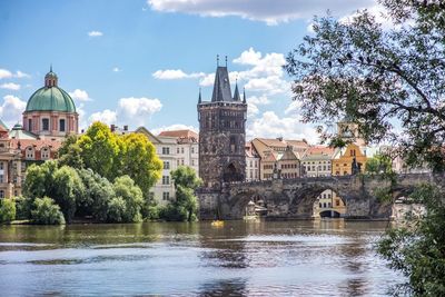 Arch bridge over river by buildings against sky