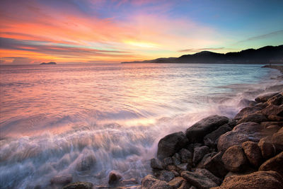 Wave splashing on rocks against sky during sunset