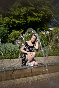 Full length portrait of a young woman sitting on fountain