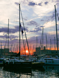 Sailboats moored in harbor against sky during sunset