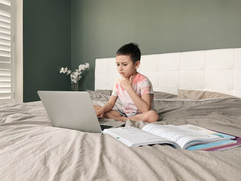 Boy using laptop while sitting on bed