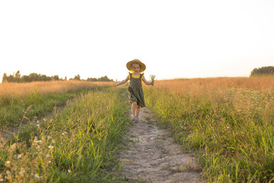 A little blonde girl in a straw hat walks in a field with a bouquet of daisies. 