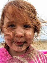 Close-up portrait of smiling girl with sand on face at beach