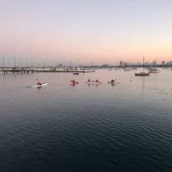 People kayaking on sea against clear sky during sunset