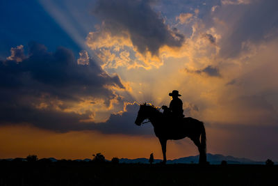 Silhouette cowboy sitting on horse at land against sky during sunset