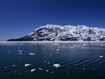 Snow floating on river by snowcapped mountain against clear blue sky