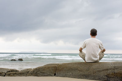Man meditating on a rock at the sea barefoot
