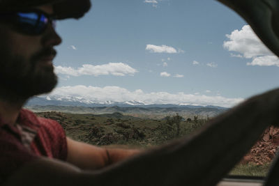 Man in car with landscape against cloudy sky in background