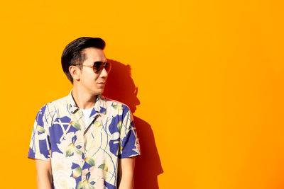 Young man wearing sunglasses standing against yellow background