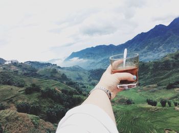 Midsection of woman holding sunglasses against mountain range