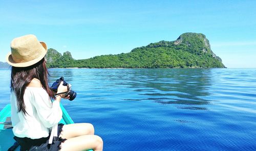 Side view of woman holding camera while sitting in boat at lake