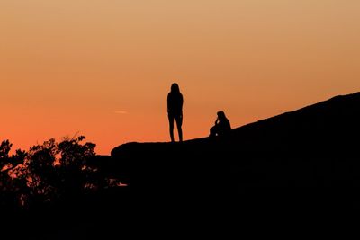 Silhouette people walking against orange sky