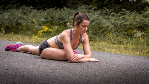 Full length of woman exercising while sitting on road