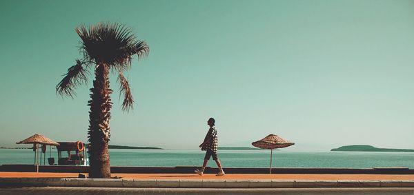 Rear view of woman standing on beach against clear sky