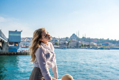 Young woman sitting against river in city