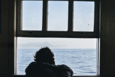 Rear view of man looking at sea seen through window