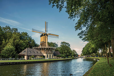 Wooden yellow windmill next to tree-lined canal at weesp. a pleasant small village in netherlands.