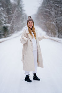 Portrait of smiling young woman standing on snow. winter fashion. warm jacket