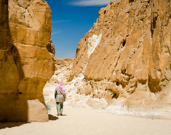 Rear view of woman walking on rock formation against sky