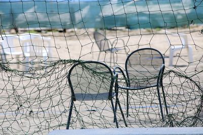 Close-up of empty chairs at beach seen through net