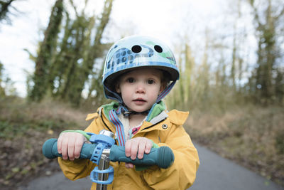 Portrait of girl with push scooter on road against sky