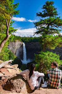 People sitting by waterfall against trees