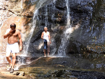 Full length of shirtless man and woman standing on rock formation