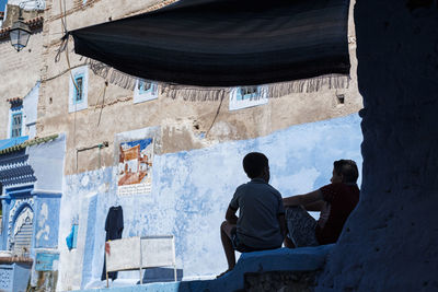 Rear view of men sitting on wall of building