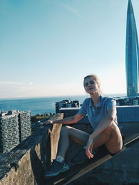 Woman sitting by sea against sky