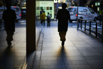 Rear view of men walking on sidewalk in city