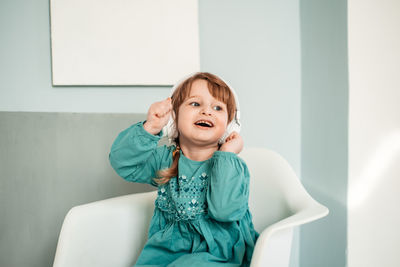 Portrait of girl sitting against wall at home