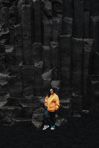 Young tourist in eyeglasses posing near high black stone wall