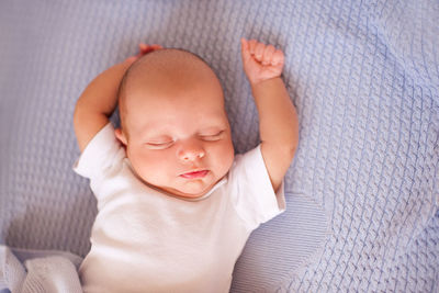 Newborn baby stretching arms on bed at home