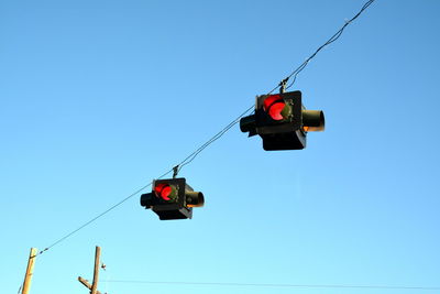 Low angle view of stoplights against clear blue sky